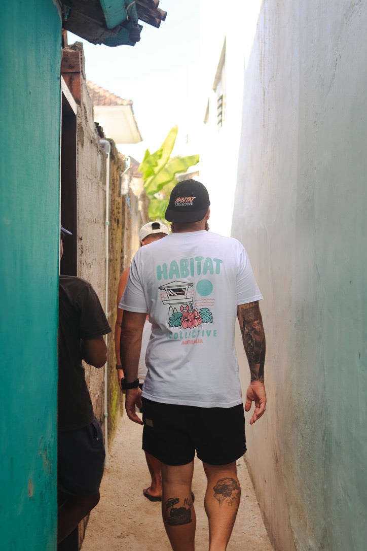 Person wearing a 'Habitat' t-shirt walking down a narrow alleyway. back view